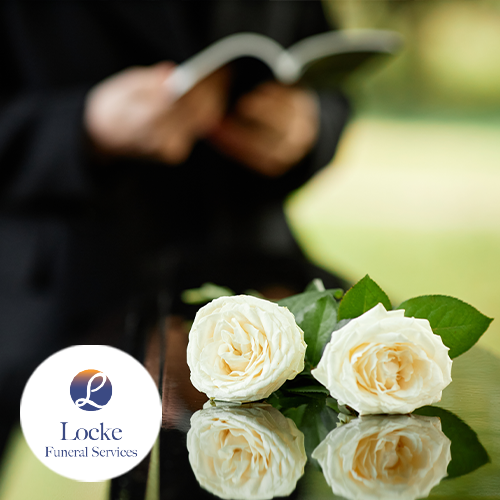Close up on white roses on a casket outdoors with person dressed in black holding a back in the blurred background